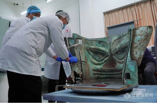 11月26日，文物修复师郭汉中（左二）带领团队为三星堆遗址3号坑出土的巨型青铜面具加固.png